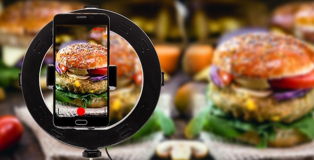 Zdjęcie burger jest filmowany za pomocą smartfona z telefonem komórkowym, który nagrywa wideo z profesjonalną jakością do aplikacji dostawy