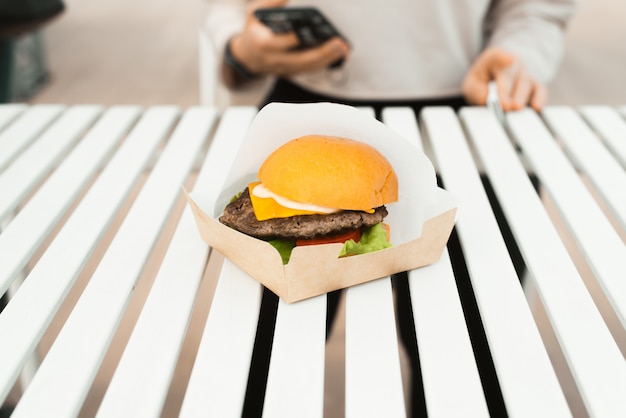 Zdjęcie burger na białym stole na zewnątrz. uliczne jedzenie na wynos w kawiarni. kotlet, ser, warzywa i sos w bułkach. selektywne skupienie