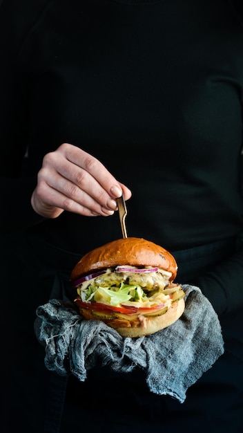 Burger w rękach szefa kuchni. Koncepcja fast foodów. Na ciemnym tle.