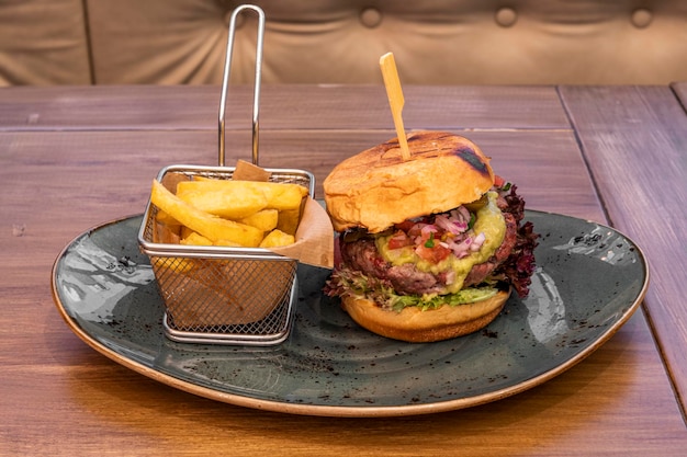 Burger w stylu meksykańskim z 200 gramami guacamole wołowego i pico de gallo oraz dodatkami ziemniaczanymi w metalowej frytkownicy na niebieskim talerzu