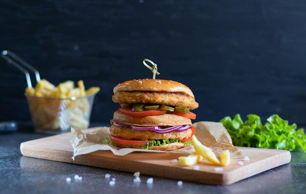 Zdjęcie burger z kurczaka z frytkami i sałatą na ciemnym tle