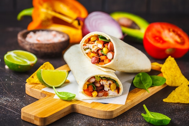 Burrito Zawija Się Z Kurczakiem, Fasolą, Kukurydzą, Pomidorami I Awokado Na Desce, Ciemne Tło. Burrito Mięsne, Meksykańskie Jedzenie.