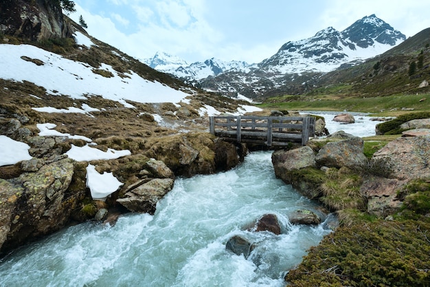 Burzliwa rzeka i drewniany most latem w Alpach (Austria).