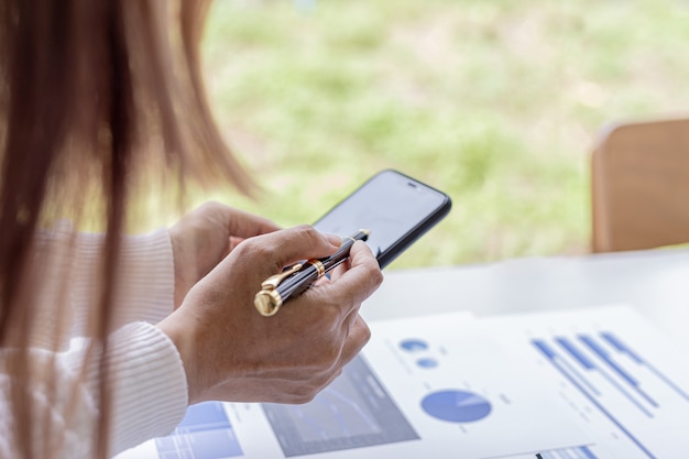 Businesswoman trzyma telefon komórkowy, patrzy na informacje na telefon komórkowy, które oficer finansowy wysyła za pośrednictwem programu do przesyłania wiadomości online. Koncepcje finansowe.