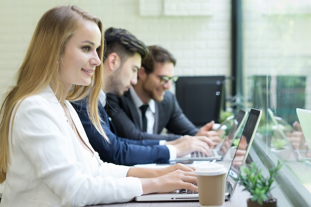 Businesswoman za pomoc? Laptopa do pracy, podczas gdy coworker interakcja w tle w biurze