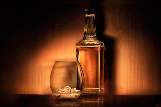 Butelka alkoholowego rumu whisky lub bourbon i szklanka z lodem na ciemnopomarańczowym tle retro st...