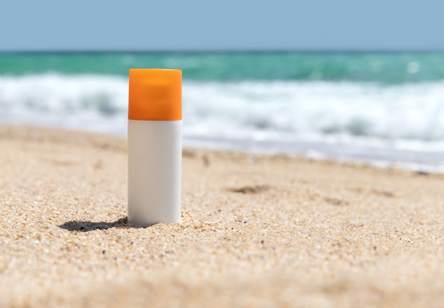Butelka balsamu do opalania na piaszczystej plaży nad morzem