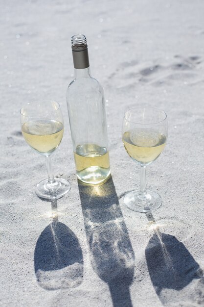 Butelka białego wina i szklanki na piasku