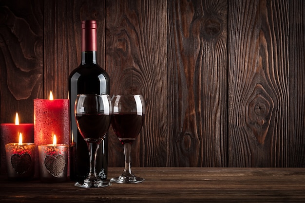 Butelka czerwonego wina, dwie szklanki wina i świece na ciemnym drewnianym tle, światło studyjne