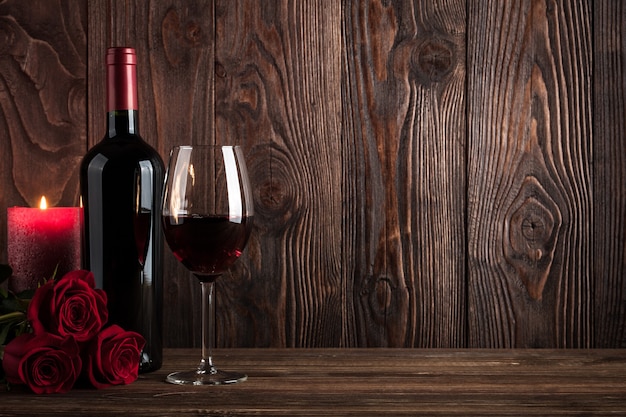 Butelka czerwonego wina, kieliszek wina, świeca i róże na drewnianym tle