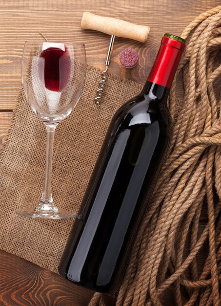 Butelka czerwonego wina, szkło, korek i korkociąg. Widok z góry na rustykalnym drewnianym stole w tle