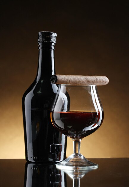 Butelka i kieliszek brandy i cygara na brązowym tle