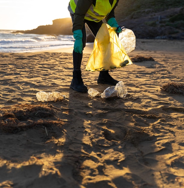Zdjęcie butelka leżąca nad brzegiem morza odebrana ręką w rękawiczce odbicie zachodu słońca nad wodą koncepcja recyklingu środowiska