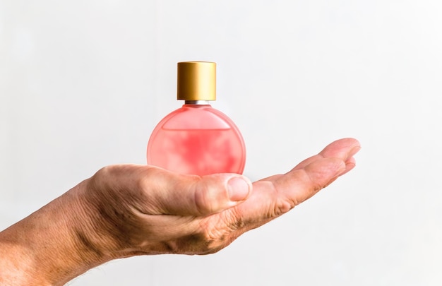 Butelka perfum damskich w męskiej dłoni na białym tle