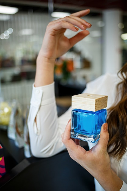 Zdjęcie butelka perfum kobiece ręka. młoda kobieta trzyma butelkę perfum. modne perfumy w rękach kobiet. dziewczyna rozpyla perfumy. piękne kobiece dłonie.