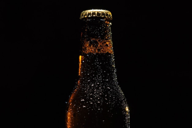 Butelka piwa z kropli wody z bliska na czarnym tle na białym tle.