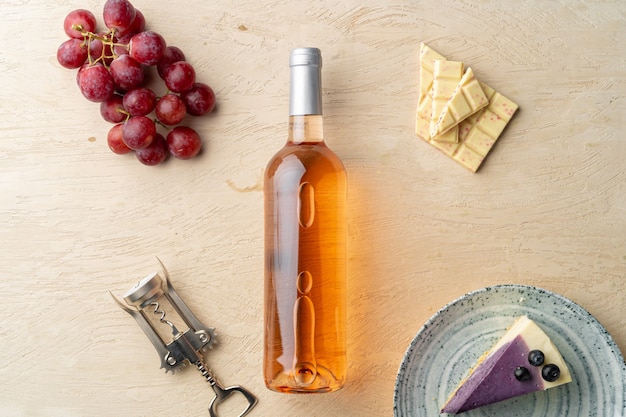 Butelka różowego wina, owoce i kawałek sernika na szarym płaskim leżaku