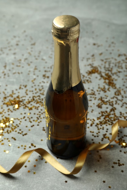 Zdjęcie butelka szampana, brokat i wstążki na szary tekstura tło.