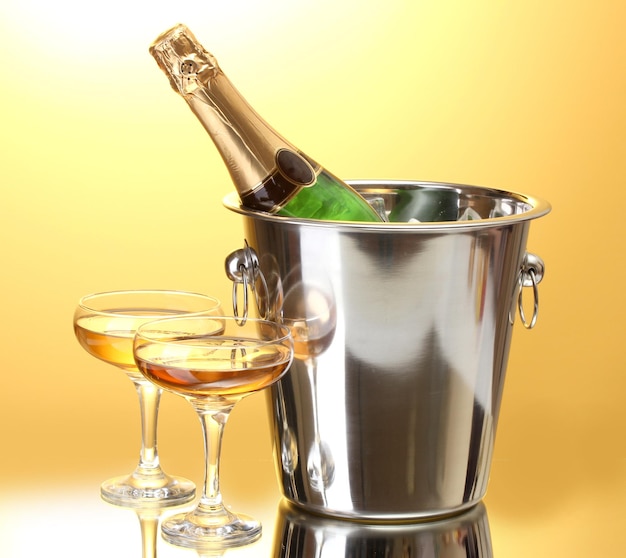 Butelka szampana w wiadrze z lodem i kieliszkami szampana, na żółtym tle