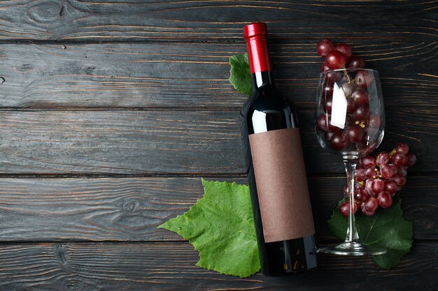 Butelka wina, kieliszek winogron i liście na drewnianym stole
