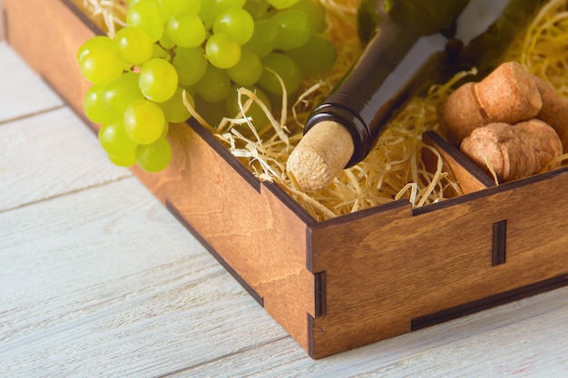 Butelka wina, korki, winogrona w drewnianym pudełku.