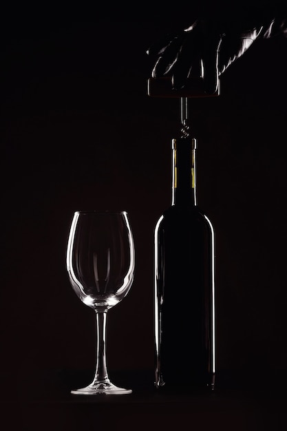 Butelka wina z kieliszkiem na czarnym tle, korkociąg