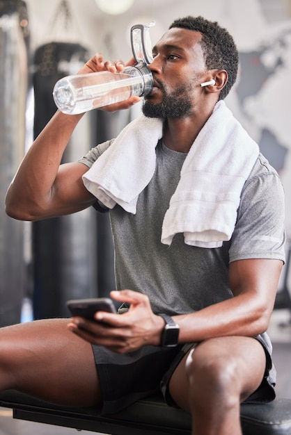 Butelka wody czarny mężczyzna w siłowni i smartfonie w mediach społecznościowych po ćwiczeniach fitness zdrowy trening sportowy i wzrost mięśni Wellness wypracuj motywację do treningu i zmęczony facet pije wodę