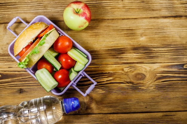 Butelka wody jabłko i pudełko na lunch z hamburgerami i świeżymi warzywami na drewnianym stole Przestrzeń kopii z widokiem z góry