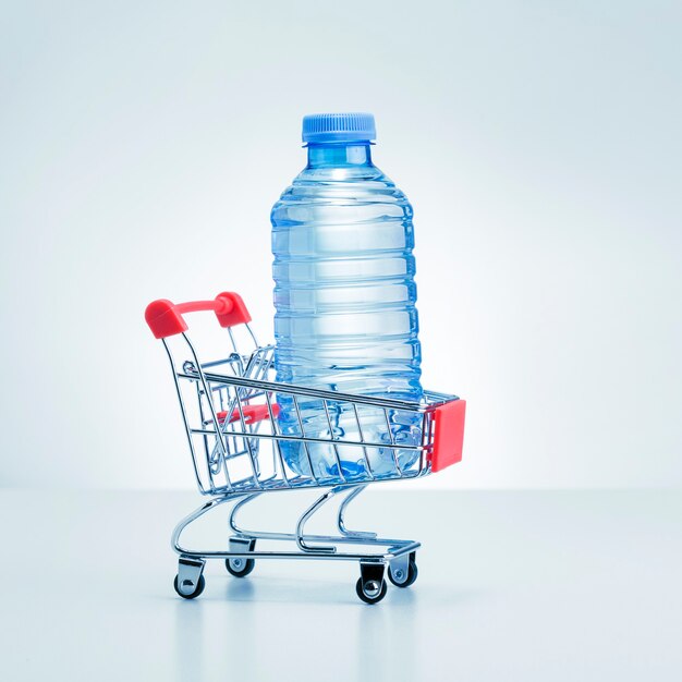 Butelka wody w wózku sklepowym na szarej powierzchni. Dostawa wody.