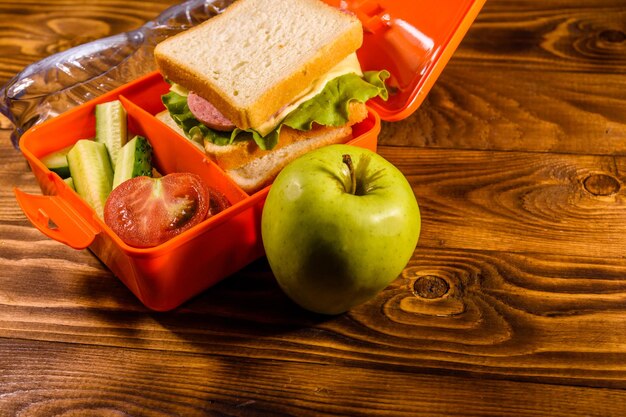 Butelka wody zielone jabłko i pudełko na lunch z ogórkami kanapkowymi i pomidorami na drewnianym stole