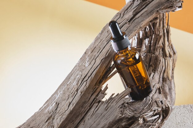 Butelka z brązowego szkła z pipetą na drewnianym korzeniu, brązowe tło, naturalne kosmetyki do pielęgnacji skóry ciała