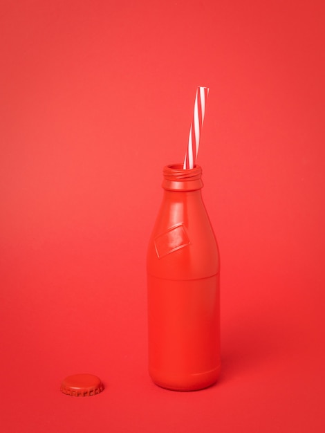 Butelka z czerwonego szkła z rurką koktajlową na czerwonej powierzchni. Pojemnik na orzeźwiające napoje.