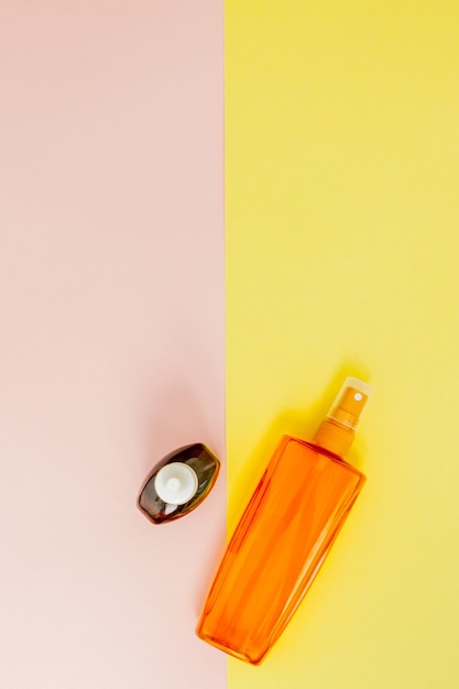 Butelka z filtrem przeciwsłonecznym na jasnej kwadratowej ścianie żółtej i różowej. Widok z góry, układ płaski, minimalizm, kopia przestrzeń.