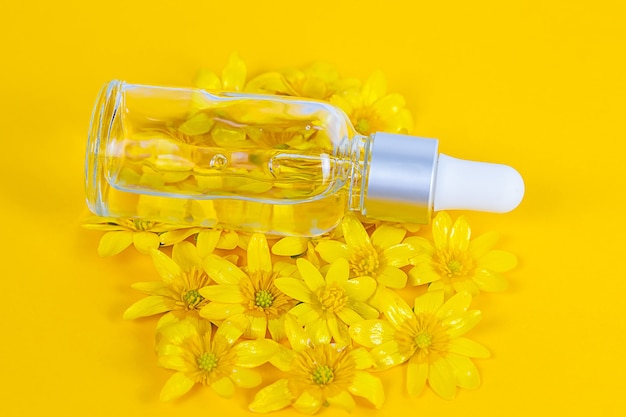 Butelka z serum do pipet na żółtym tle w otoczeniu wiosennych kwiatów