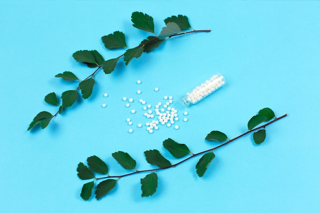 Butelka z tabletkami homeopatycznymi i zielonymi liśćmi roślin