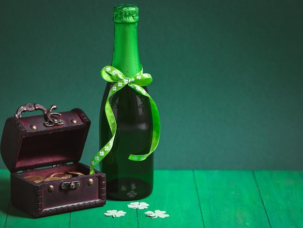 Butelka zielonego piwa z wstążką zawiązaną w łuku półotwarta skrzynia z monetami i koniczyną papierową