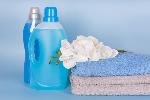 Butelki Detergentu I Zmiękczacza Do Tkanin Z Czystymi Ręcznikami I Kwiatami Orchidei Na Niebieskim Tle