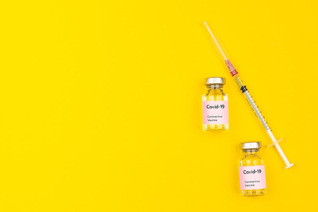 Butelki i strzykawki ze szczepionką Covid-19 koronawirusem połączone na żółtym tle z miejscem na kopię. Widok z góry i płaskie ujęcie.