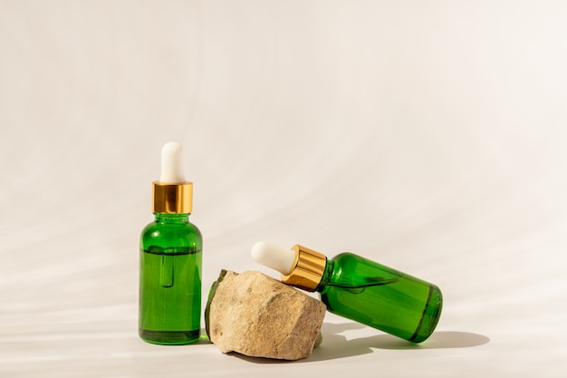 Butelki kosmetyczne z zielonego szkła z zakraplaczem na beżowej powierzchni z kamieniem