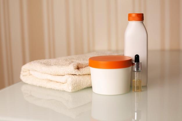 Butelki szamponu, serum i odżywki do włosów z ręcznikiem kąpielowym na biurku na neutralnym beżowym tle. Miejsce na tekst