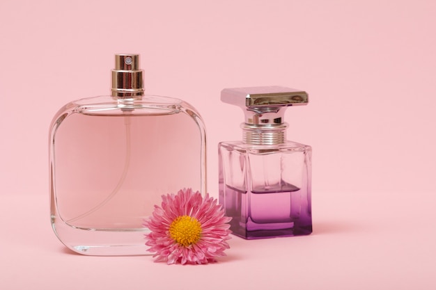 Butelki z damskimi perfumami i pączkiem kwiatów na różowym tle. Produkty dla kobiet.