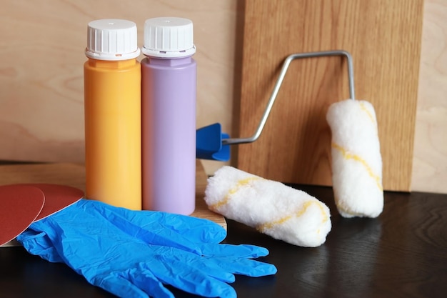 Zdjęcie butelki z farbą malują rolkowe niebieskie rękawiczki i papier ścierny przedmioty potrzebne do naprawy na drewnianym stole