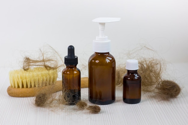 Butelki z lekami i szczotka do włosów na białym drewnianym stole Problem wypadania włosów