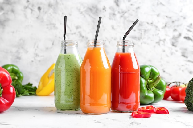 Butelki zdrowego smoothie z różnymi warzywami na jasnej powierzchni