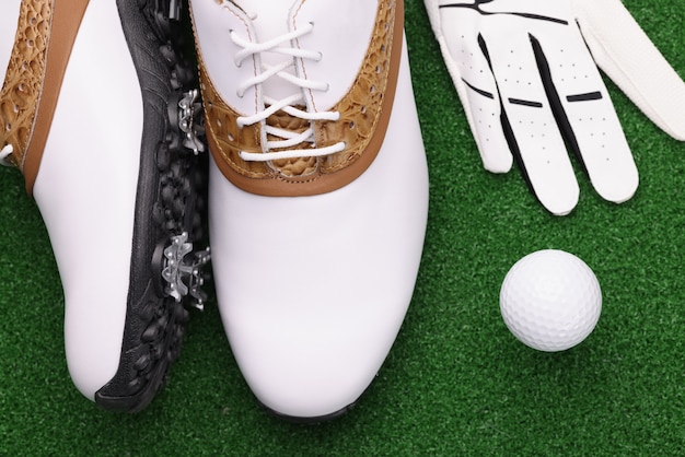 Buty golfowe, piłka i białe rękawiczki leżą na zielonym trawniku