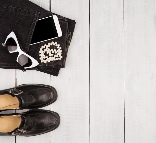 Buty i dżinsy smartfon okulary perłowe na białym drewnianym biurku
