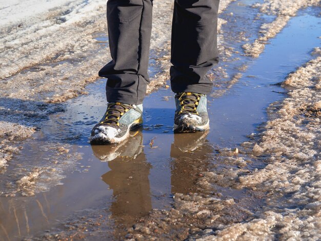 Buty trekkingowe na błotnistą wiosnę. Lód topnieje na wiosnę, człowiek idzie przez kałuże na ulicy, wiosenna pogoda.