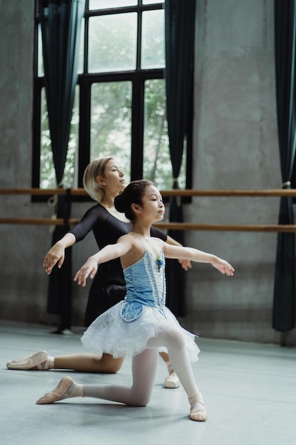 Całe ciało z boku azjatyckiej dziewczyny powtarzającej ruchy baletowe z osobistym instruktorem w klasie tańca Sto