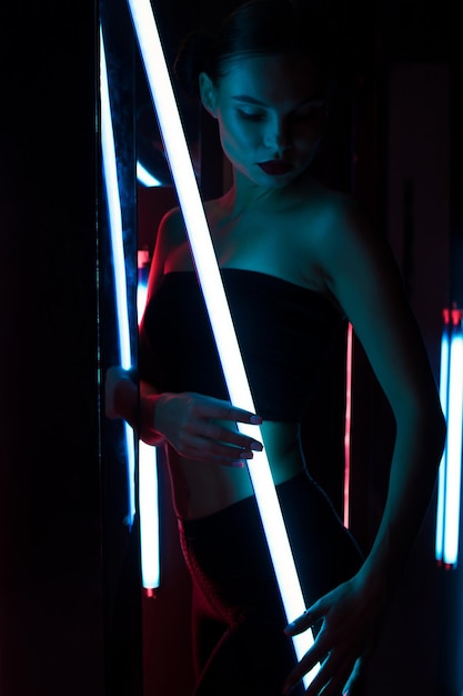 Całe ciało zmysłowa kobieta z jasną lampą opartą o ścianę w ciemnym pokoju z neonowym oświetleniem