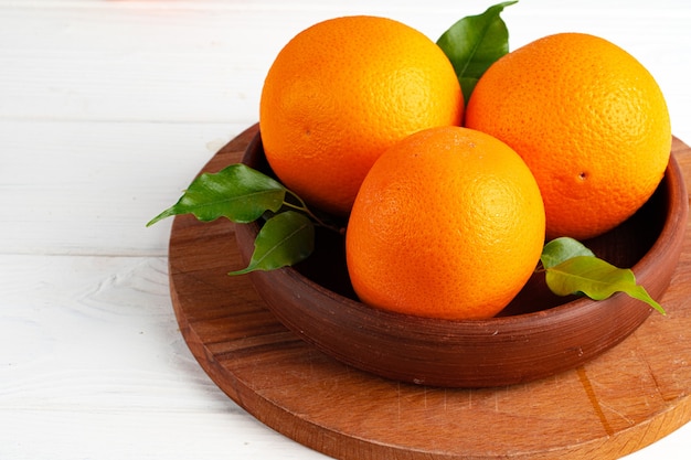 Całe dojrzałe pomarańcze w glinianej misce na białym stole